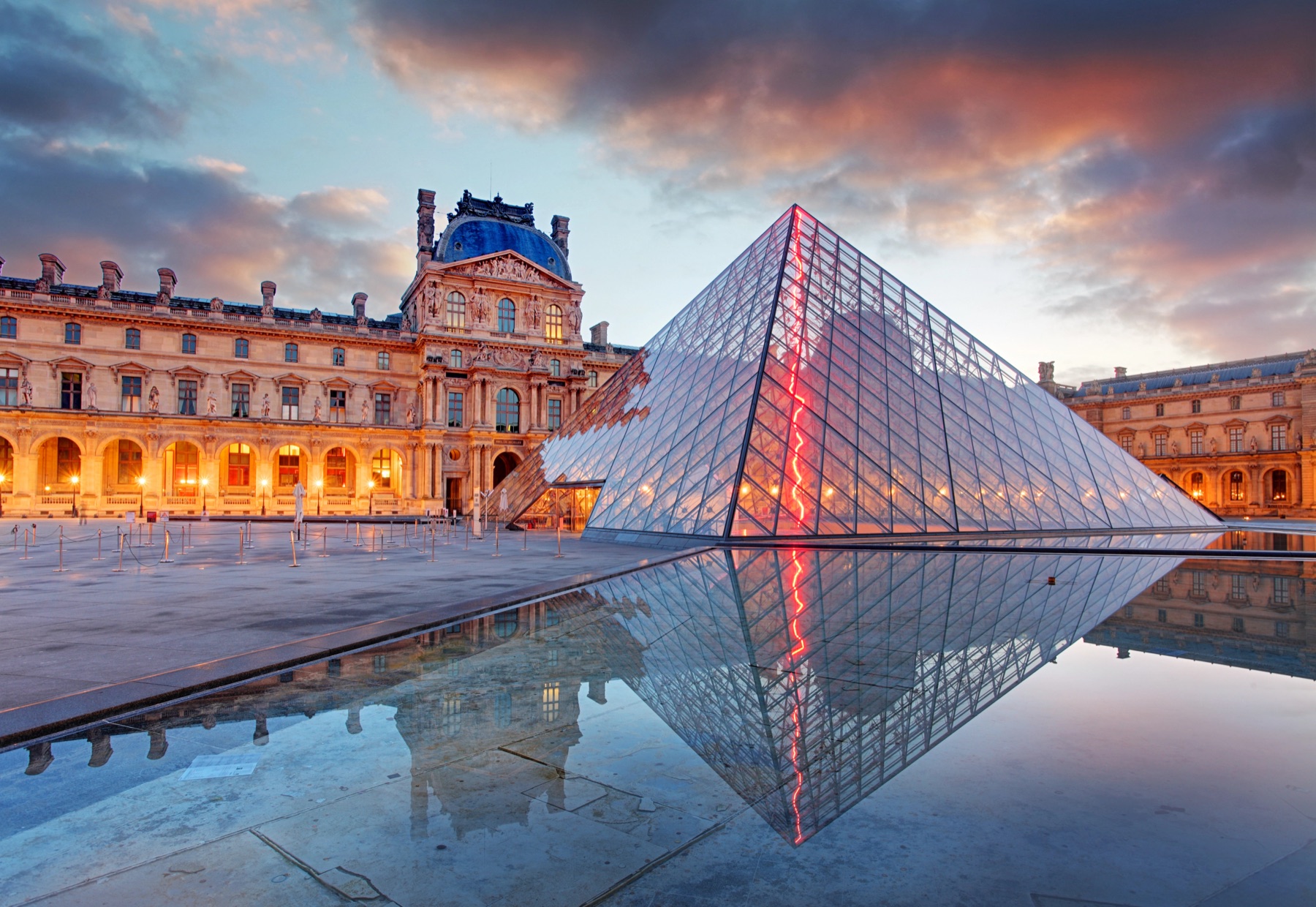 The Louvre's glass Pyramid lit at dusk, mirrored in the courtyard pool, Paris