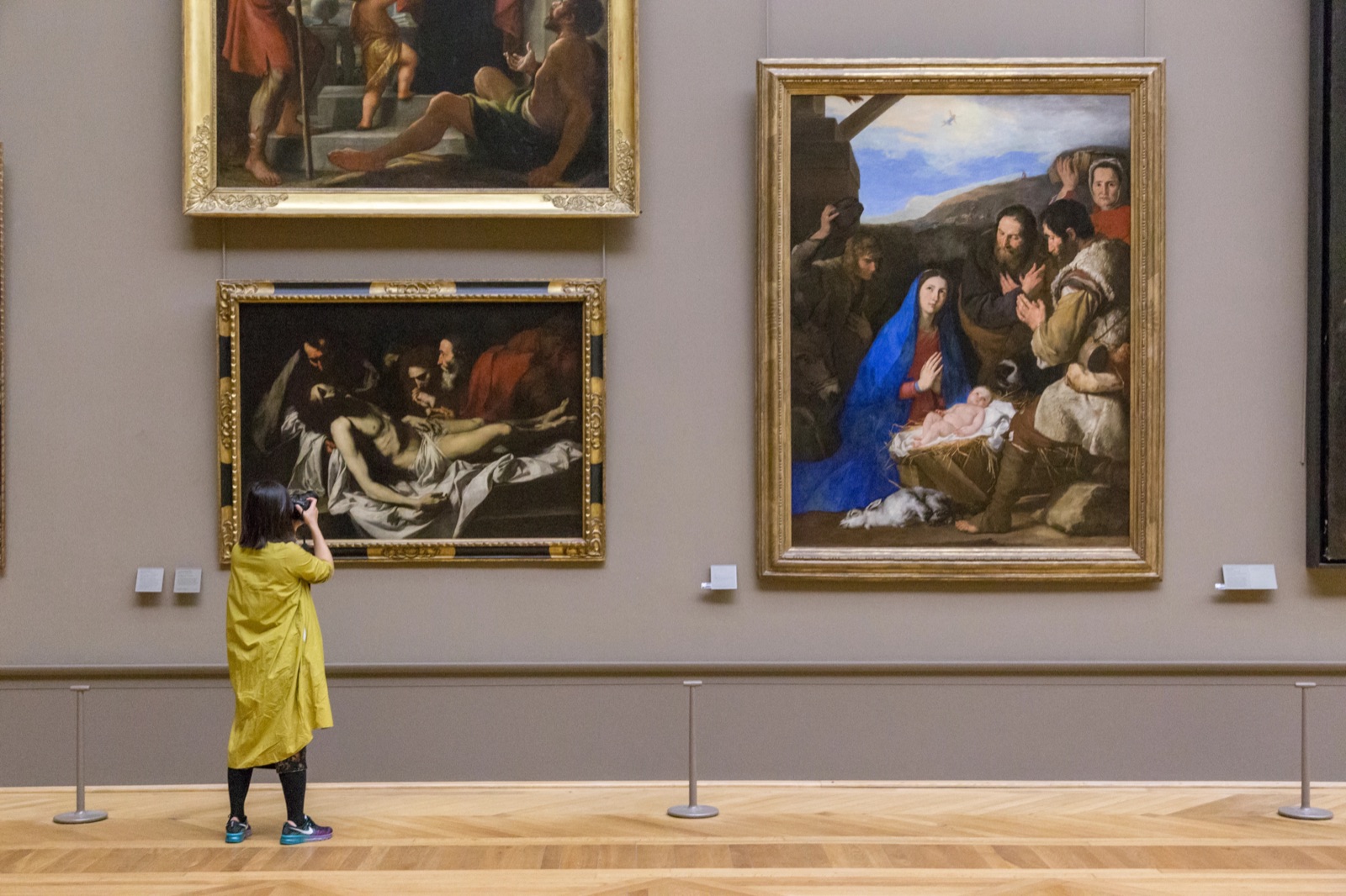 A visitor photographing old master paintings in a quieter Louvre gallery